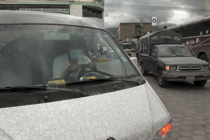 A man wears a surgical mask while driving his car covered in volcanic ash in Machachi