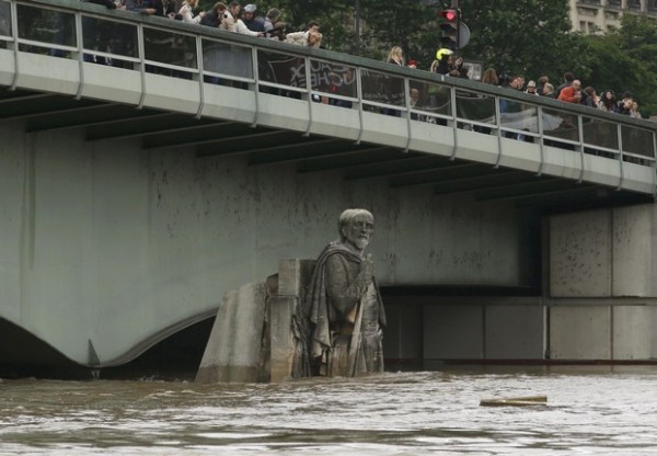 People stand on the Pont de l'Alma as they look at the Zouave statue covered by the rising waters from the Seine River after days of rainy weather in Paris