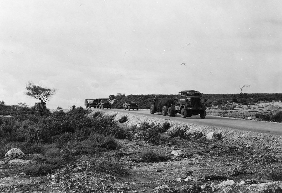The bomb is then escorted to the nearby North Field airbase on Tinian, shrouded in tarp.